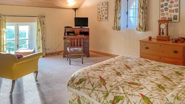 A bedroom with a bed, a desk, a chair, a dresser, a clock, and a window with curtains.