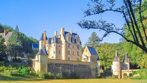 A large, historic castle with multiple towers and a well-maintained lawn in front.