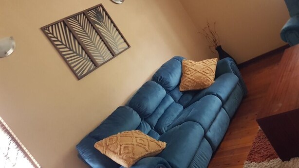 A living room with a blue sofa, two patterned cushions, a wooden coffee table, and a decorative wall piece. - Repose Airbnb (Qonce)