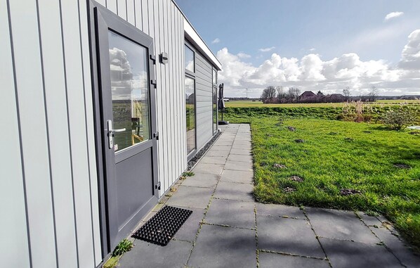 Een modern gebouw met een grijze gevel, een glazen deur en een verharde looppad naar een grasveld.