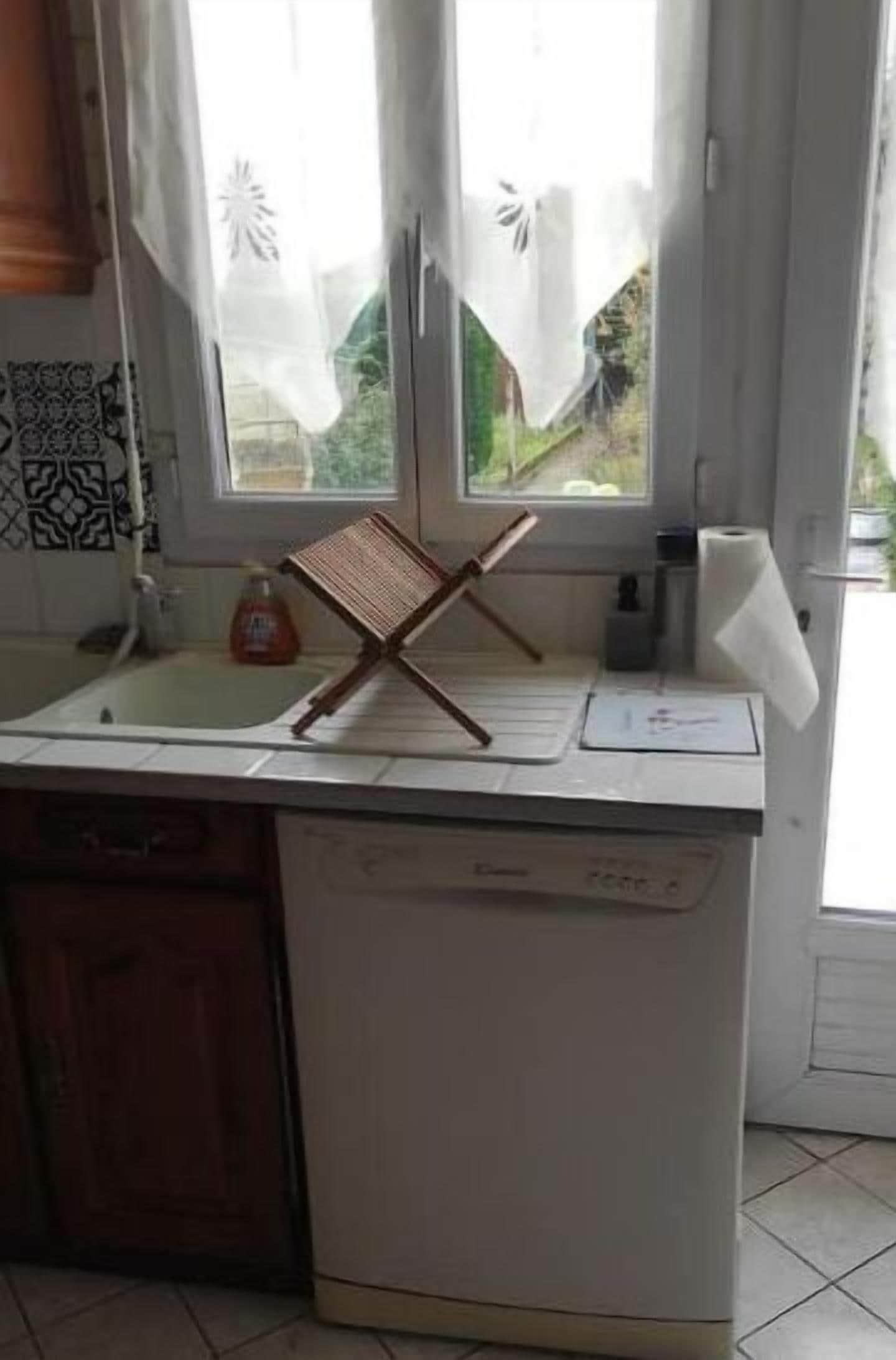 Eine Küche mit weißer Arbeitsplatte, einem Holzstuhl, einem Fenster mit Vorhängen und einem Spülbecken.
