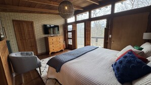 Un dormitorio con una cama grande, techo de madera, televisión y vistas por las ventanas.