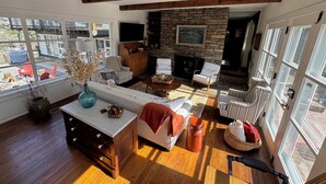 Amplia sala de estar con chimenea de piedra, vigas de madera y ventanas grandes.