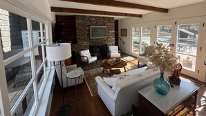 Una sala de estar acogedora con chimenea de piedra, vigas de madera y ventanas amplias.