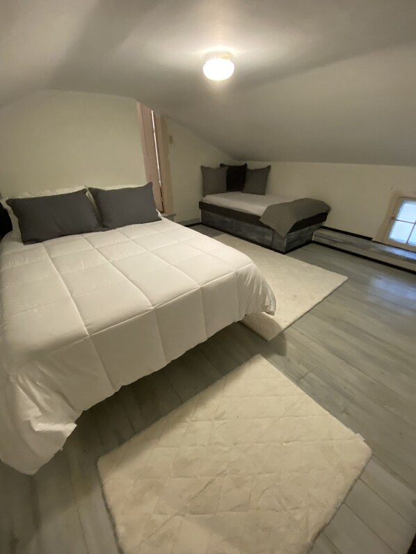 Une chambre avec un grand lit, un plus petit lit et un tapis blanc.