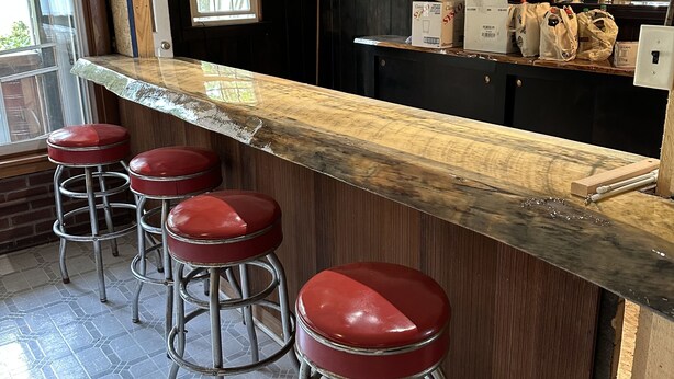 A bar area with a wooden counter, four red stools, and a window with blinds.