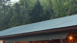 A covered outdoor area with a metal roof, wooden pillars, and a gravel path.