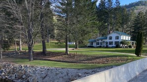 A large white house with a green roof, surrounded by trees and a stone wall.