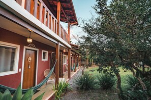 A red building with a wooden balcony, a hammock, and a garden with various plants. - Pousada Sertão (Alto Paraíso de Goiás)