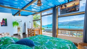 A bedroom with a bed, a desk, and a view of a coastal landscape.