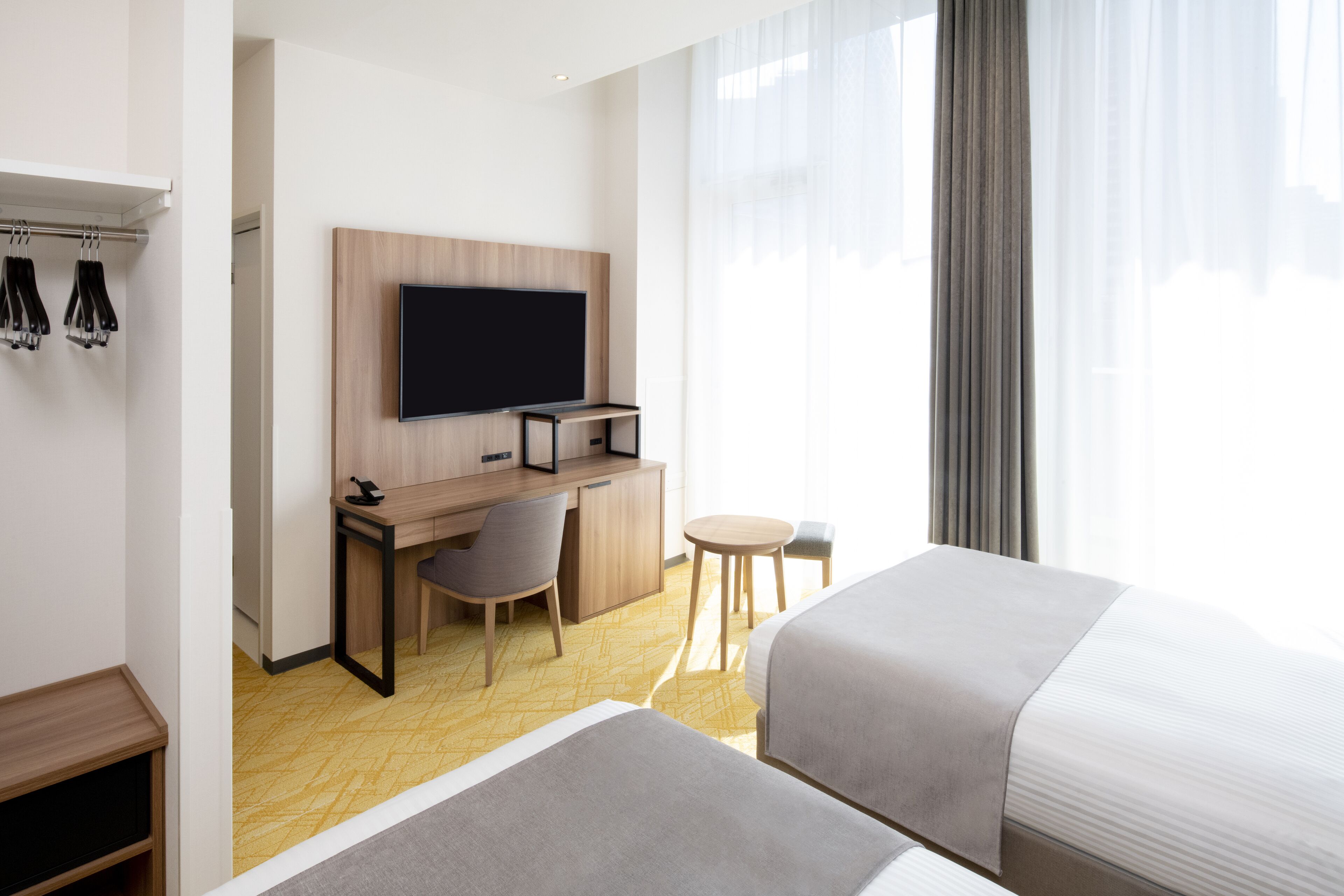 A hotel room with a bed, a desk with a chair, a television, and a small table.