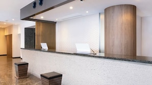 Una moderna reception con un bancone in marmo, due cestini alti di colore scuro e una parete rivestita in legno.