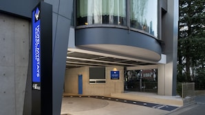 Ingresso moderno di un hotel, con insegna blu che indica il nome dell'hotel e una rampa accessibile per carrozzina.