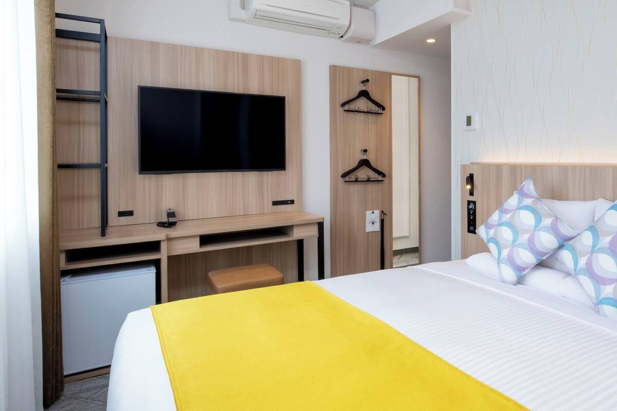 Hotellihuone, jossa on sänky, televisio, työpöytä ja vaatekaappi.