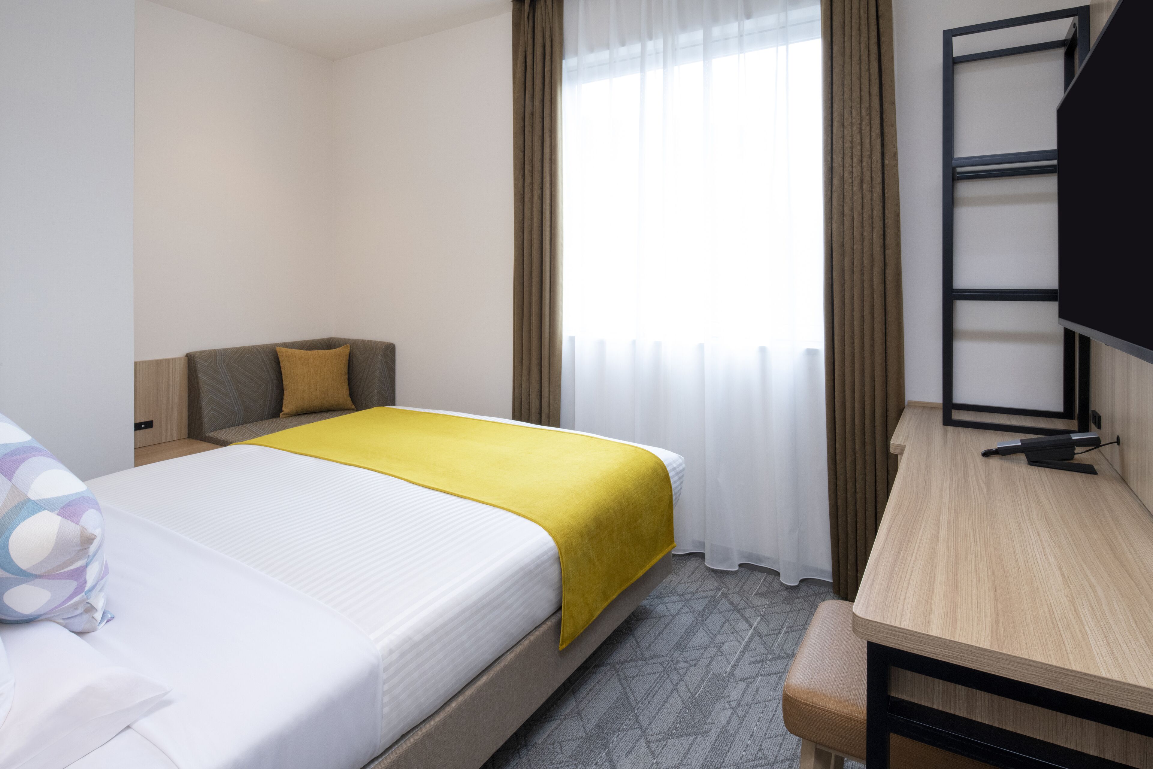 Ein Hotelzimmer mit einem Bett, einem Schreibtisch, einem Fernseher und einem fenster mit Vorhängen.