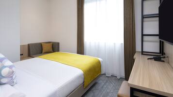 Ein Hotelzimmer mit einem Bett, einem Schreibtisch, einem Fernseher und einem fenster mit Vorhängen.