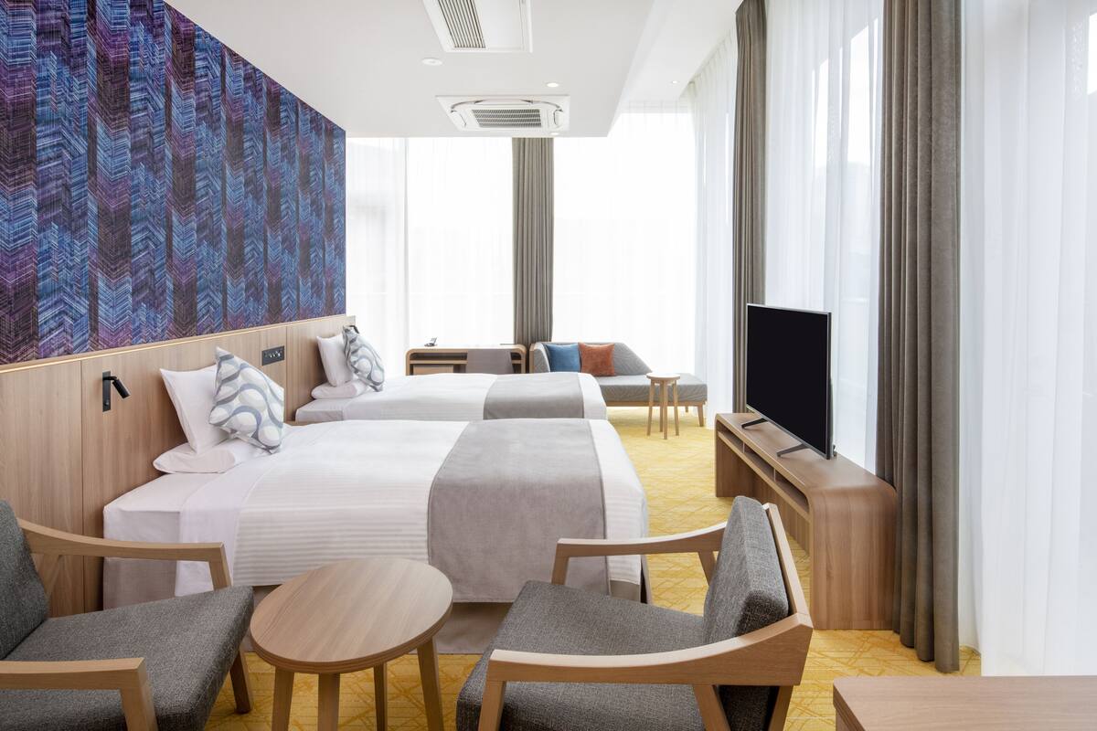 Hotellihuone, jossa on kaksi sänkyä, televisio, työpöytä ja sohva.