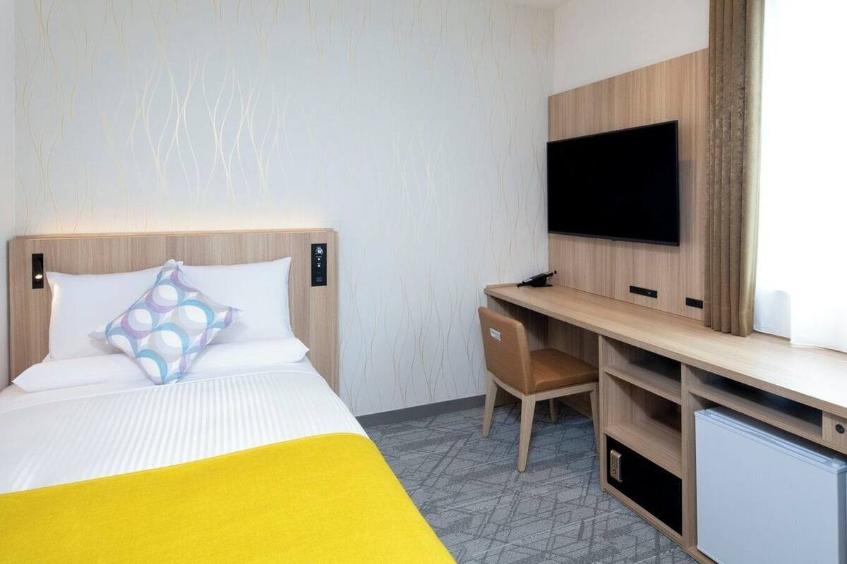 Hotellihuone, jossa on sänky, työpöytä, tuoli, televisio ja pieni jääkaappi.