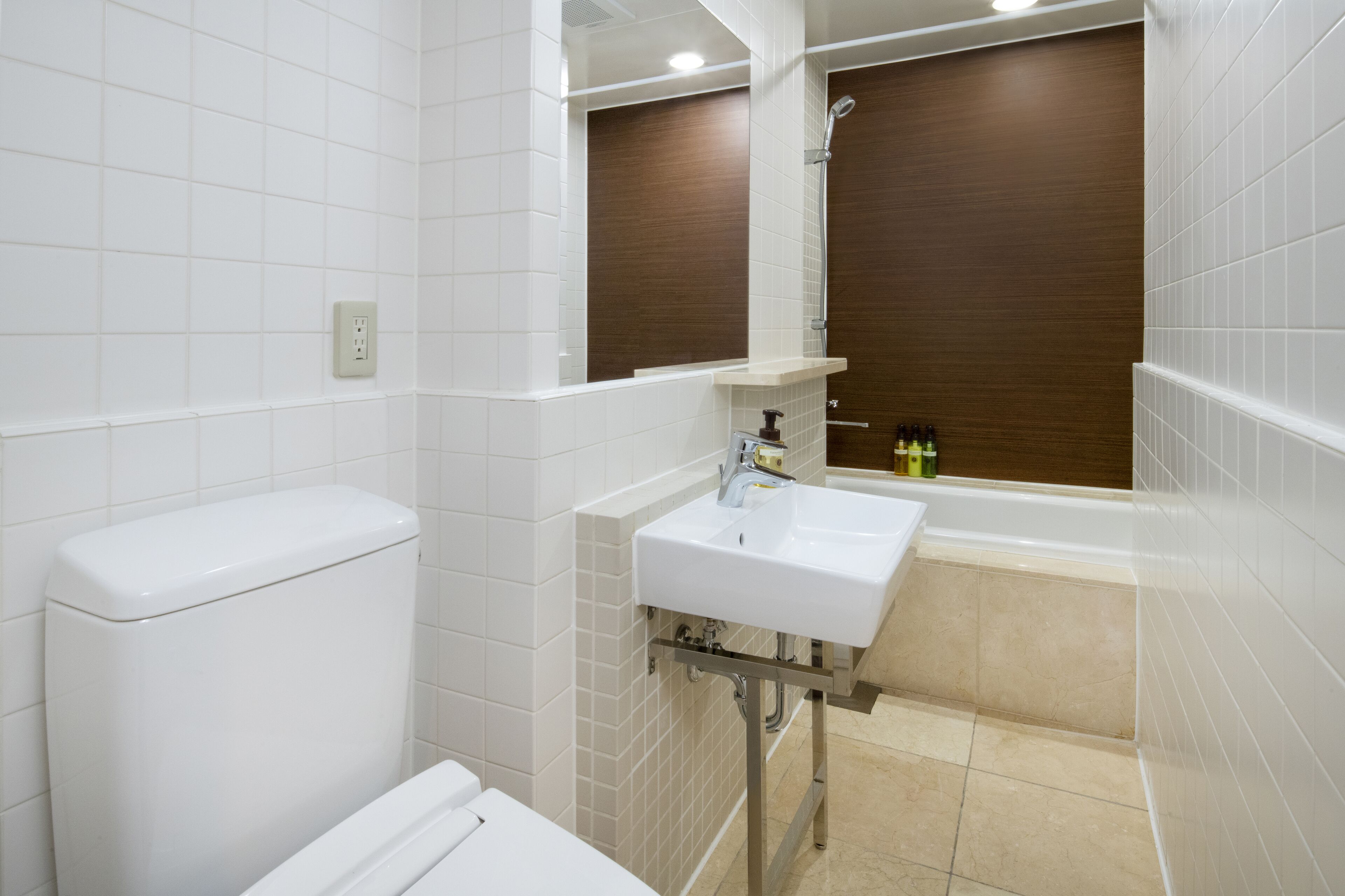 Une salle de bain moderne avec des carreaux blancs, des toilettes blanches, un lavabo avec un miroir et une baignoire.