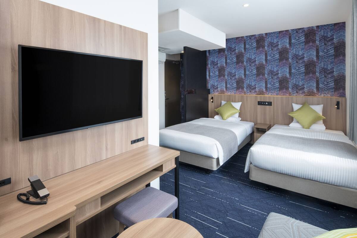 Hotellihuone, jossa on kaksi sänkyä, televisio, työpöytä ja kuviollinen seinä.