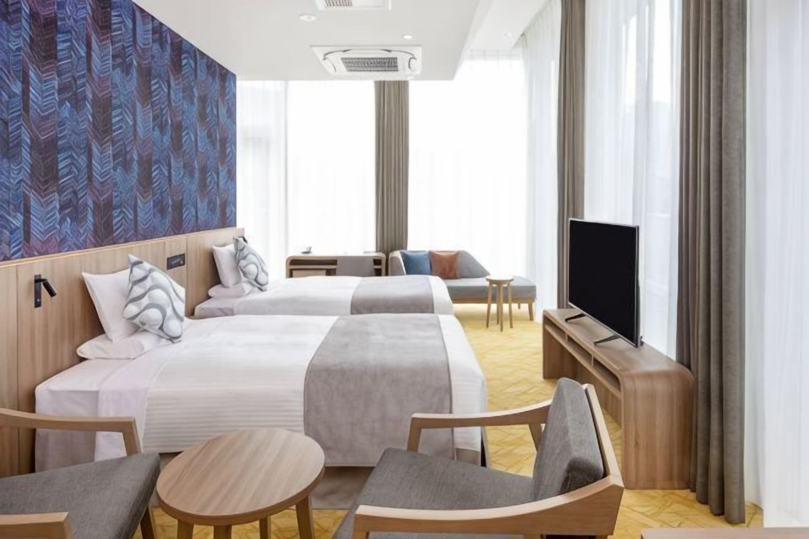 Una camera d'albergo con due letti, una televisione, un divano, una scrivania e una sedia.