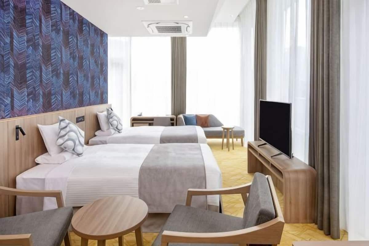 A hotel room with two beds, a TV, a sofa, a desk, and a chair.