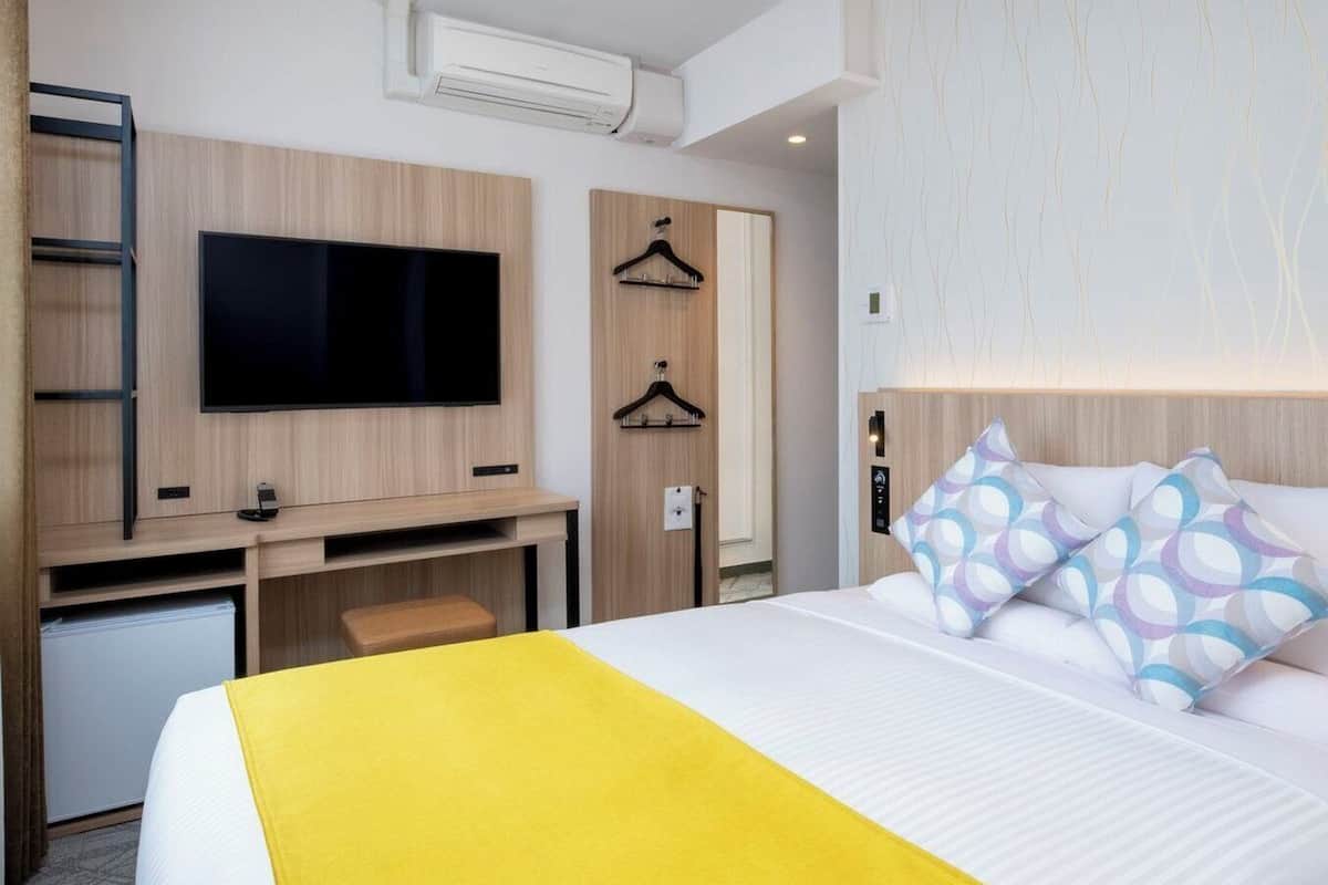 Hotellihuone, jossa on sänky, työpöytä, jossa on televisio, vaatekaappi ja naulakko.