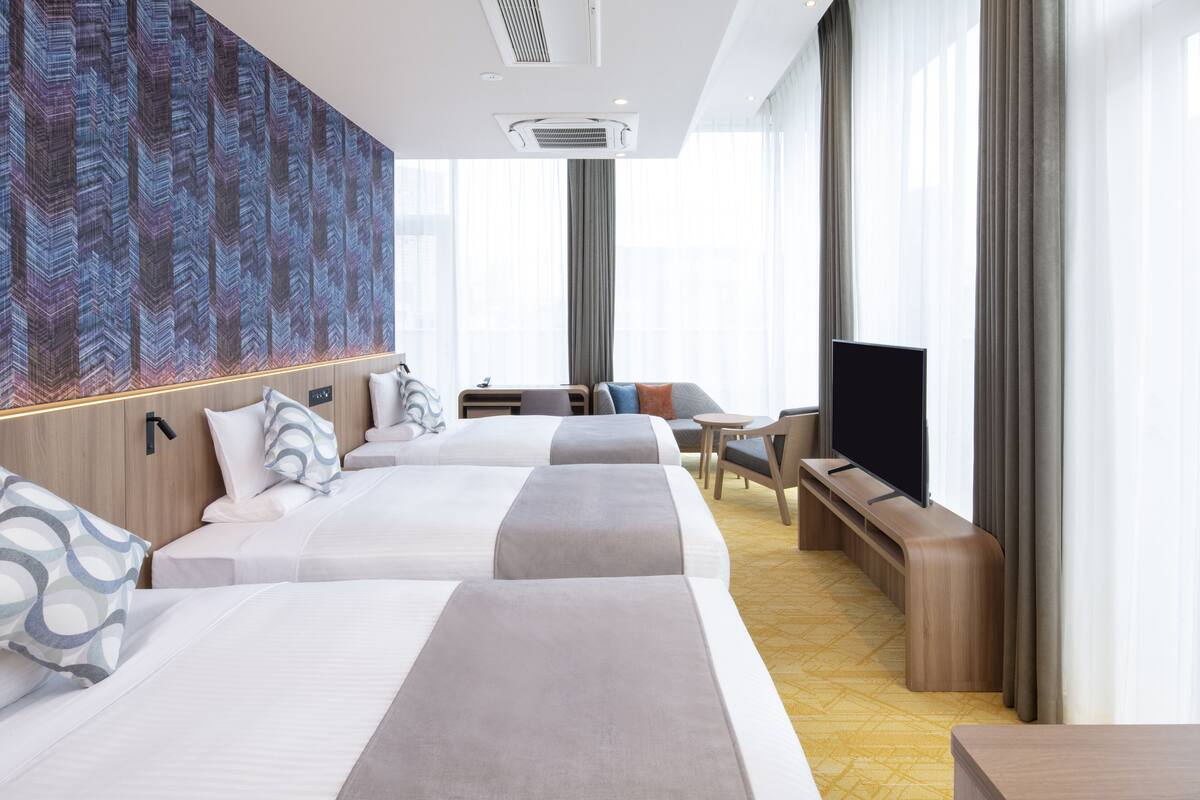 Hotellihuone, jossa on kaksi sänkyä, televisio, sohva ja pieni pöytä.
