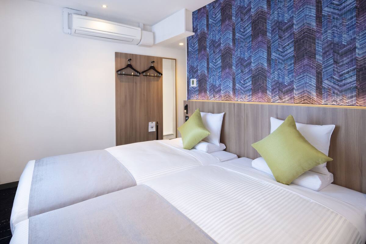 Hotellihuone, jossa on suuri sänky, kaksi tyynyä, puinen pääty ja seinä, jossa on geometrinen kuvio.