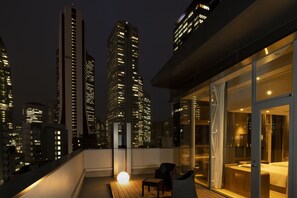 A high-rise building with illuminated windows at night, a balcony with a wooden floor, and a glass-enclosed room with a bed and seating area. - HOTEL MYSTAYS Nishi Shinjuku (Tokyo)