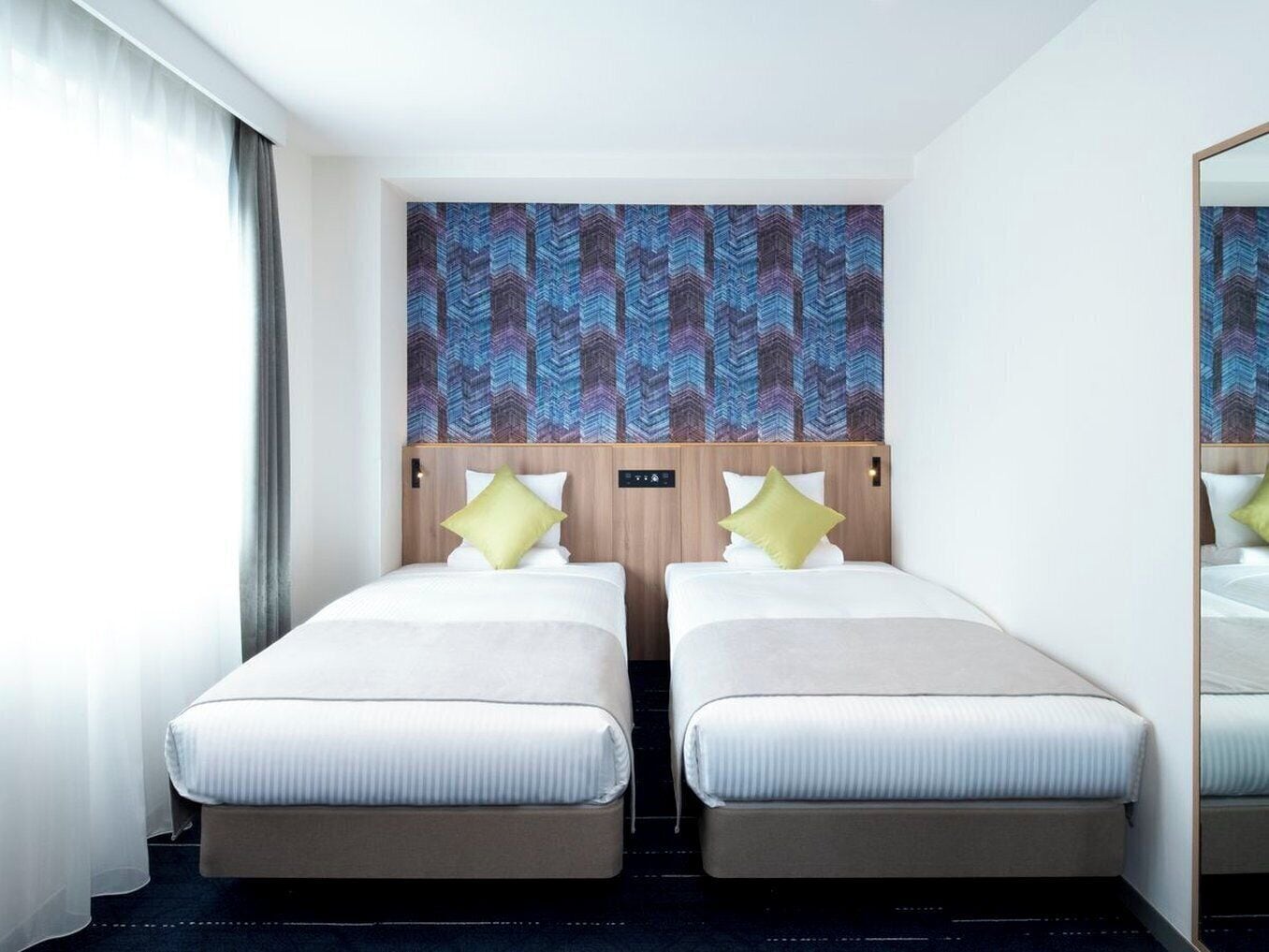 Hotellihuone, jossa on kaksi erillistä sänkyä, suuri peili ja kuvioitu seinä sänkyjen yläpuolella.