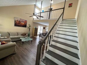 A living room with a staircase, a ceiling fan, and a painting on the wall.