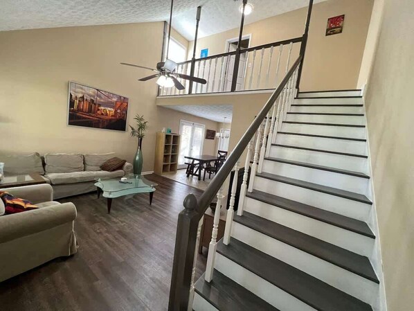 Una sala de estar con escaleras, un ventilador de techo y un cuadro en la pared.