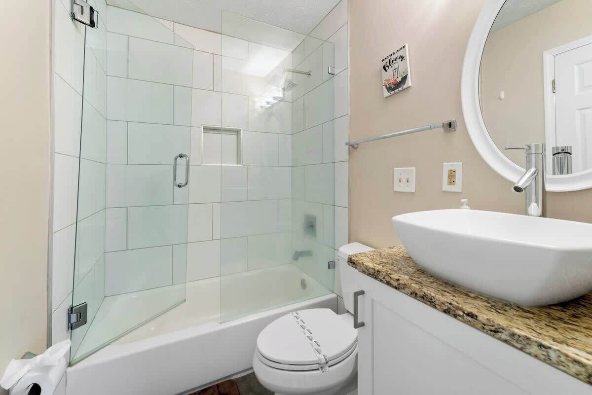 A bathroom with a glass-enclosed shower, a white toilet, and a sink with a granite countertop.