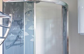 Un coin de pièce avec une cloison en verre ornée de motifs de feuilles, une rambarde métallique et un mur recouvert de carreaux blancs.