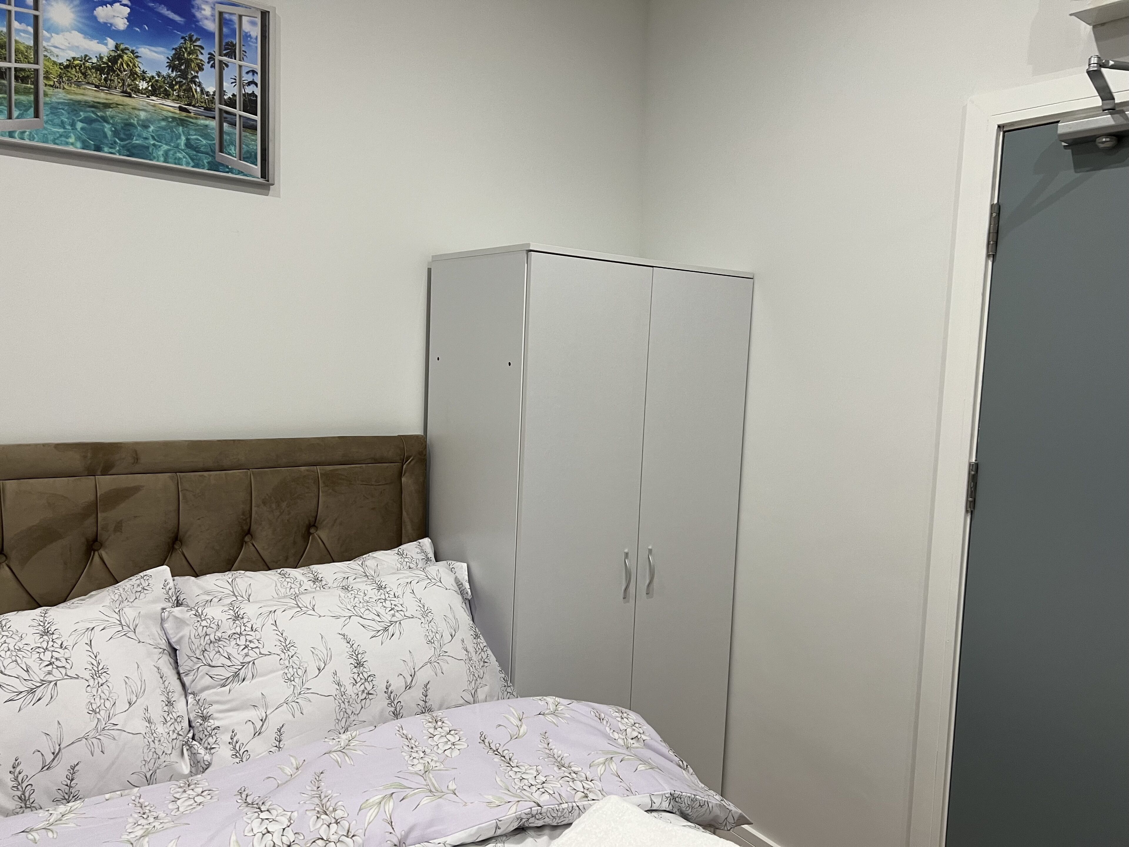 Quarto com cama, guarda-roupa e pintura de uma praia tropical.