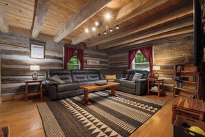 Interior de una cabaña de madera con un sofá, dos sillones, una mesa de centro y una chimenea.