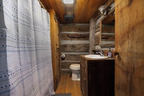 A rustic wooden bathroom with a toilet, sink, and shower curtain. - "Timber Lodge", Rustic 4BR Log Cabin + Guesthouse (Bluff City)