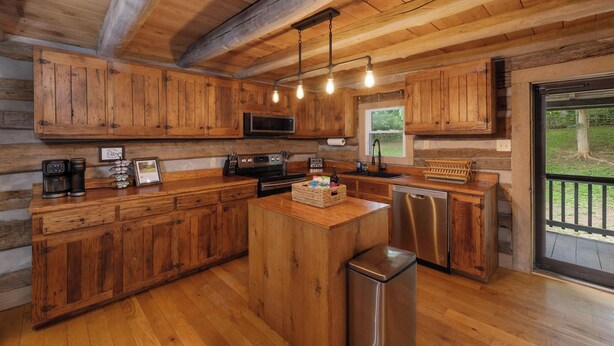 A wooden cabin-style kitchen with a central island, built-in microwave, and stainless steel appliances. - "Timber Lodge", Rustic 4BR Log Cabin + Guesthouse (Bluff City)