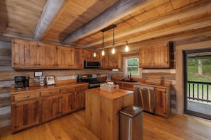 A wooden cabin-style kitchen with a central island, built-in microwave, and stainless steel appliances. - "Timber Lodge", Rustic 4BR Log Cabin + Guesthouse (Bluff City)