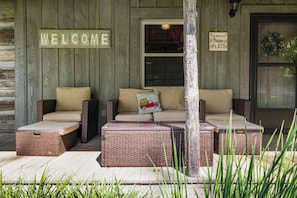 A porch with wicker furniture, a welcome sign, and a sign stating 'This porch is my happy place.' - "Timber Lodge", Rustic 4BR Log Cabin + Guesthouse (Bluff City)