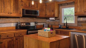 A rustic kitchen with wooden cabinets, a built-in microwave, a stainless steel stove, and a wooden island with a basket of items. - "Timber Lodge", Rustic 4BR Log Cabin + Guesthouse (Bluff City)