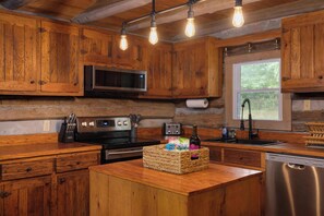 A rustic kitchen with wooden cabinets, a built-in microwave, a stainless steel stove, and a wooden island with a basket of items. - "Timber Lodge", Rustic 4BR Log Cabin + Guesthouse (Bluff City)