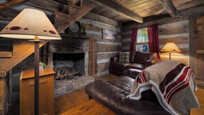 A log cabin interior with a fireplace, leather sofa, and plaid curtains. - "Timber Lodge", Rustic 4BR Log Cabin + Guesthouse (Bluff City)