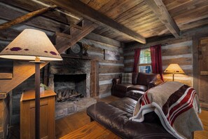 Ein Holzblockhaus-Interieur mit Kamin, Ledersofa und karierten Vorhängen.