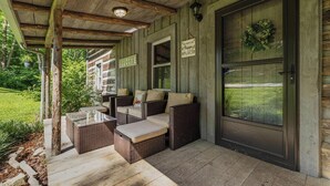A covered porch with wicker furniture, a welcome sign, and a door with a wreath. - "Timber Lodge", Rustic 4BR Log Cabin + Guesthouse (Bluff City)
