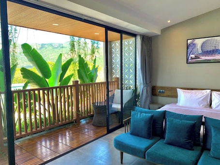A room with a bed, a sofa, a small table, and a balcony with a wooden railing and plants.. The Mystery Con Dao