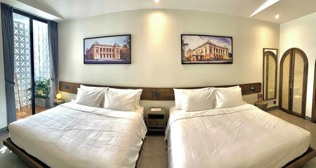 A hotel room with two beds, a nightstand, a lamp, and two framed pictures on the wall.