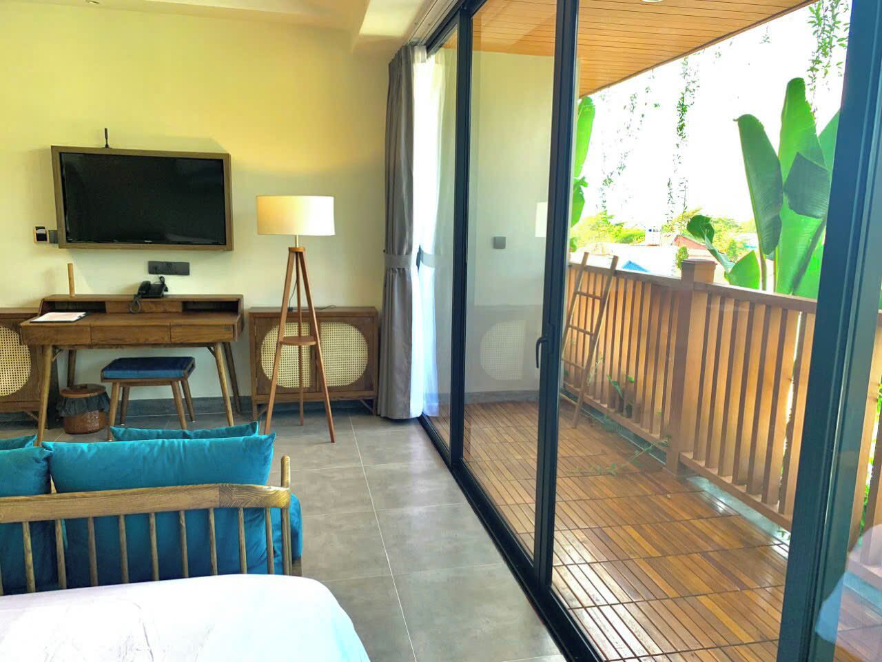 A room with a bed, a desk, a television, and a balcony with a wooden railing.