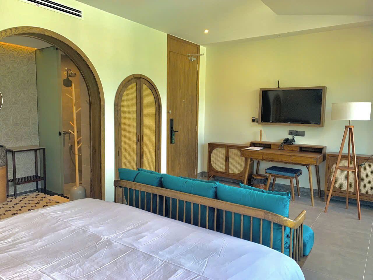 Una habitación de hotel con cama, zona de estar con cojines, escritorio con silla, televisor y ventana.